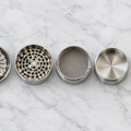 Alle Teile des HIZEN Edelstahl Grinders: Deckel mit Wellen-Mahlwerk, Mahlkammer, Pollensieb, Pollenkammer, Pollenschaber und Dosierlöffel